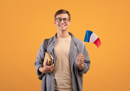éducation européenne, étude moderne ou étudiant d'échange. jeune mec heureux dans des verres avec sac à dos, bloc-notes et petit drapeau de la france, isolé sur fond orange, espace de copie, prise de vue en studio Banque d'images