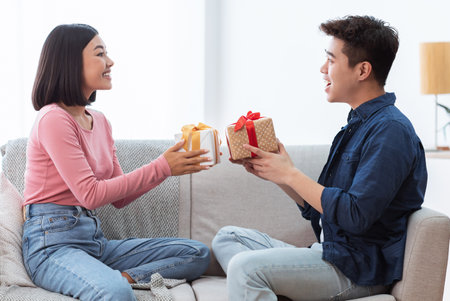 Célébration de la saint-valentin. beau couple asiatique donnant des boîtes-cadeaux se félicitant mutuellement célébrant les vacances ensemble assis sur un canapé à la maison. romance, vacances présente concept Banque d'images