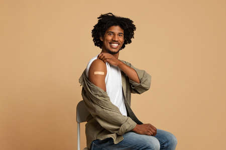 Handsome vaccinated black guy showing arm with adhesive bandage after coronavirus vaccination