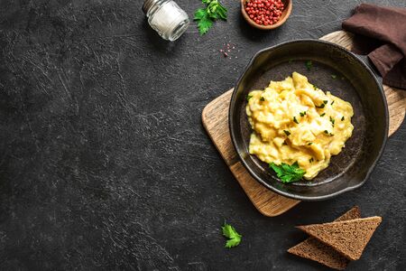 Oeufs brouillés sur une poêle à frire pour un petit-déjeuner ou un brunch sain, vue de dessus, espace de copie. recette de repas maison - œufs brouillés sur fond noir.