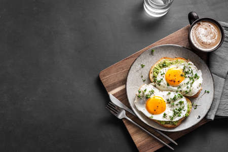 Sandwichs aux œufs d'avocat pour un petit-déjeuner sain. toasts à grains entiers avec purée d'avocat, œufs au plat et micro-verts biologiques sur table sombre, espace de copie.