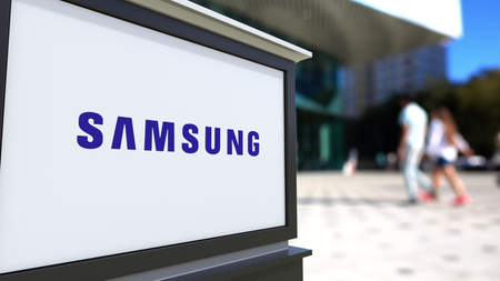 logo samsung: Street signage board with Samsung logo. Blurred office center and walking people background. Editorial 3D rendering United States