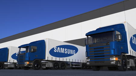 logo samsung: Freight semi trucks with Samsung logo loading or unloading at warehouse dock. Editorial 3D rendering