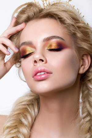 Retrato de joven hermosa mujer rubia con trenzas modernas maquillaje creativo y la espina de pescado que llevan corona de oro. ojos ahumados multicolores y las cejas perfectas