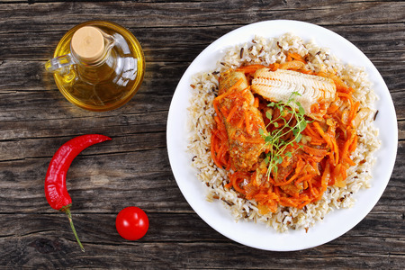 煮込み美味しい白身魚の部分とニンジン タマネギ トマト スパイス ハーブ野生とレモンの切れ端でまな板の上の白いプレートに長粒米を添えて 上からの眺め の写真素材 画像素材 Image