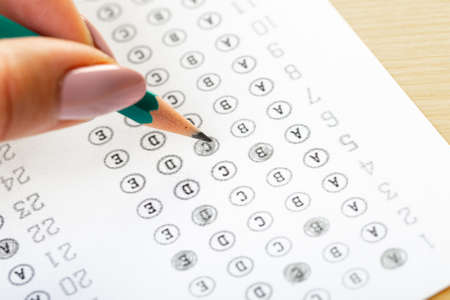 The student fills in the answers to the test in the exercise and examination paper with a pencil. computer worksheet with pencil in school test room, education concept.
