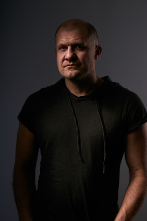 Depression angry crime man with bald head looking mystery and agressive in black shirt on dark grey background. closeup portrait.