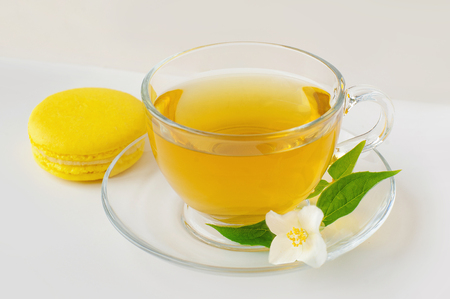 Tea cup with green tea, fragrant Jasmine flowers, tea leaves and Macaroon in the white background Фото со стока