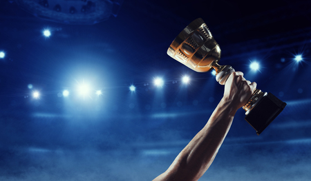 Hand of athlete holding cup trophy against stadium. mixed media