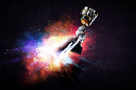 Hands holding champion cup on colourful splashes background. mixed media