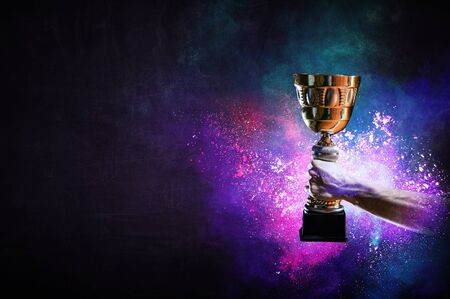 Hand holding up a gold trophy cup against dark background Stock Photo