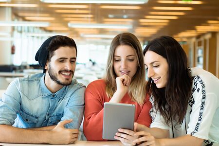 University students sitting together at table using digital tablet. Group study in university library.  Education concept