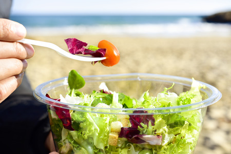 Gros plan d'un jeune homme caucasien, manger une salade préparée à côté de la mer Photo