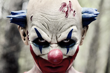 Closeup of a scary evil clown with a disturbing look in his eyes in the woods