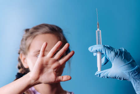 The girl does not want to be vaccinated. against vaccination. bad vaccine. girl holds hand near face protest against vaccine next to doctor's hand with syringe with vaccine, medicine.angry and distrustful patient refuses to receive it.