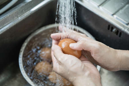 Femme au foyer asiatique méconnaissable lavant un œuf cru dans l'évier en gros plan, femme désinfectant et préparant une coquille d'œuf sale avant de cuisiner dans la cuisine. Banque d'images