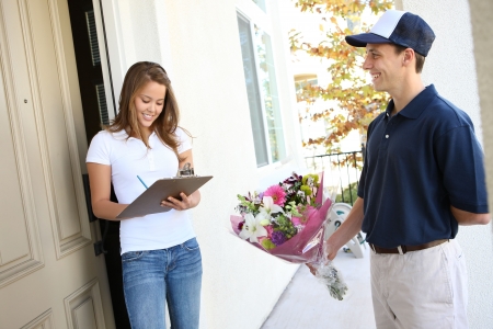 A delivery man giving flowers to pretty woman at home Фото со стока