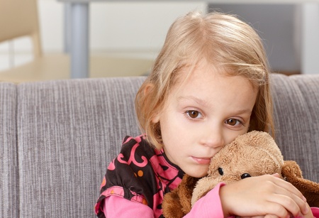sad lonely: Lonely little girl sitting sadly on sofa at home, hugging plush toy. Stock Photo