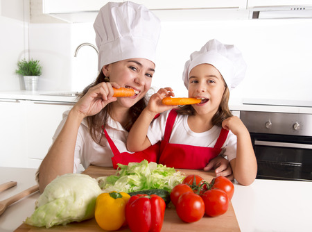 a carrot: hạnh phúc của mẹ và đứa con gái nhỏ trong chiếc tạp dề và nấu mũ chuẩn bị salad và ăn cà rốt với nhau có vui vẻ tại bếp nhà cười vui tươi trong dinh dưỡng thực vật khỏe mạnh và khái niệm giáo dục Kho ảnh