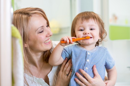 smiling mother and kid son brushing teeth in bathroom