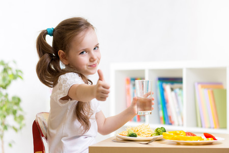 Kindermädchen isst das gesunde Lebensmittel, das sich Daumen zeigt