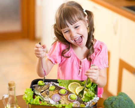 Lustiges Kindermädchen und gegrillte Fische an der Küche. Meeresfrüchte mit gesundem Essen.