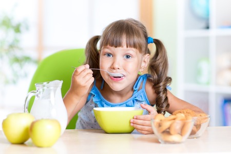 nettes Kindermädchen, das Getreide mit Milch in der Baumschule isst Foto auf Lager