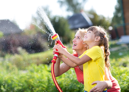 Portrait of little gardener girl with mother watering on lawn near house
