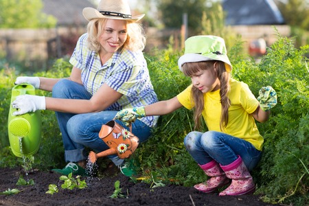 Mother and Daughter Child Watering Plants in Garden.