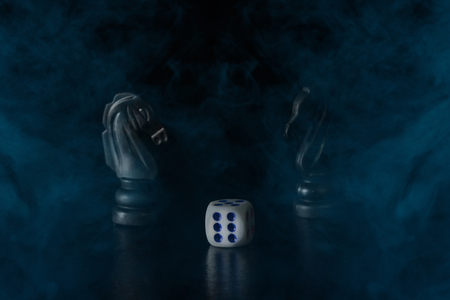 Objects for board games dice and two black horses in blue cigarette smoke on a dark background concept of hobby and passive recreation