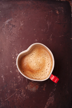 coffee in unusual vintage tin mug with red handle on old metal backdrop in heart shape Stock Photo