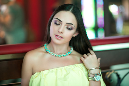 Fashion look young beautiful lady, yellow dress without shoulders, green neck lace, stylish gold and silver expensive wrist watch. walking through big city center shops, holiday best shopping time Stock Photo