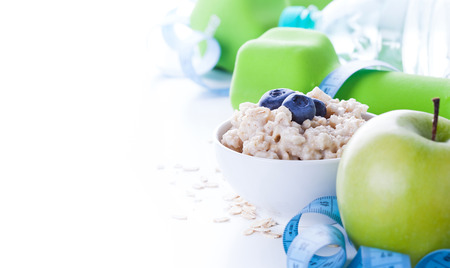 Cadre de fitness avec petit-déjeuner énergétique, flocons d'avoine, pomme et eau minérale avec outils de sport en arrière-plan. Concept de mode de vie sain avec espace de copie.