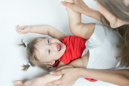 Funny Baby Girl Doing Exercise And Yoga With Her Happy Mother On A White Bed Funny Baby Girl Doing Exercise And Yoga With Her Happy Mother On A White Bed