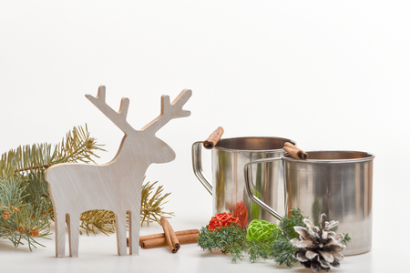 hot drink of mulled wine or tea with cinnamon spice stick in metallic mug near decorative wood deer and straw balls at christmas isolated on white background, copy space