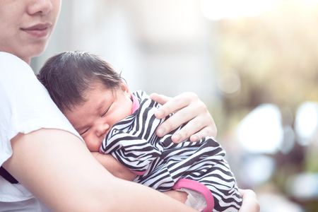 かわいいアジアの新生児の女の子は 母親の胸の上に眠っています 若い母親が優しさで赤ちゃんを抱きしめる の写真素材 画像素材 Image