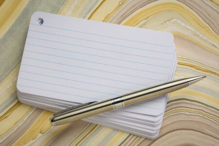 stack of blank index card with a pen over wavy marbled paper