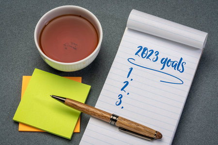 2023 goals list in a notebook with pen and reading glasses, setting New Year goals and resolutions Banco de Imagens