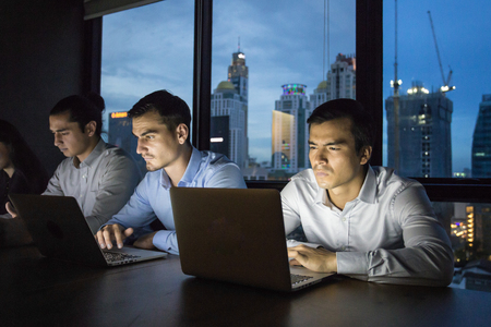 business team working late at night with lights off and computers laptop screen light on. Business people working hard concept. 20-30 year old. Stock Photo - 79412211