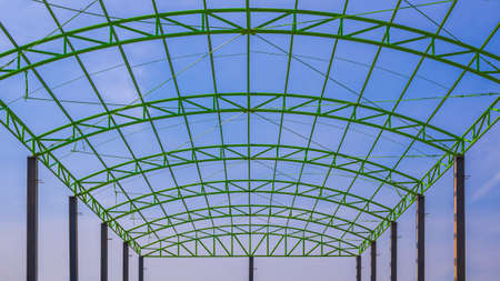Low angle view of green metal roof structure of industrial building against blue sky in construction site