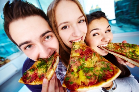 Bild von den glücklichen Jugendfreunden, die Pizza essen und Kamera betrachten Foto auf Lager