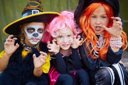 portrait of three little girls in halloween costumes looking at camera with frightening gesture stock photo