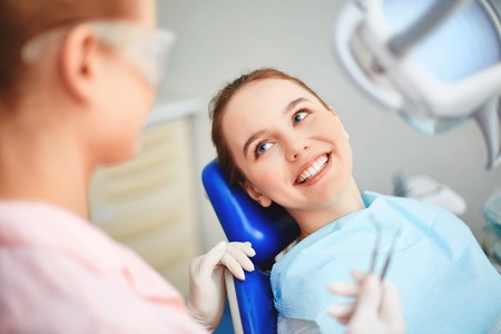 Joven mujer sentada en el consultorio del dentista y mirando a su doctor con sonrisa Foto de archivo - 39635333