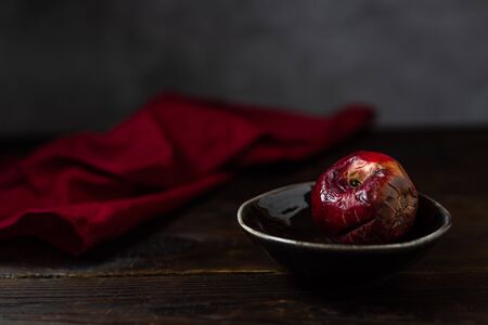 Art concept of the problem of food consumption. red rotten apple on a plate with tehstil on a wooden table and a gray background. minimalistic still life in a dark style of paintings by artists. Stock Photo