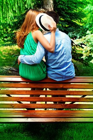 young people tenderly kissing on a park bench love concept stock