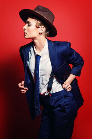 男のスーツと帽子でポーズ 魅力的な若い女性の肖像画 男のスタイルの服 背景が赤です ファッションを撮影しました の写真素材 画像素材 Image