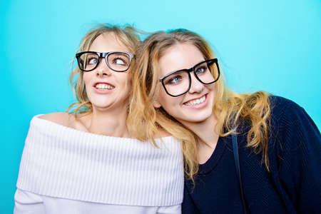 two pretty cheerful girls in glasses make faces in studio over