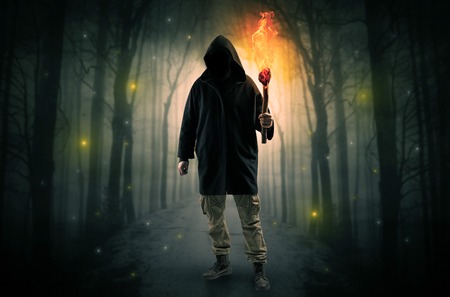 Mysterious man coming from a path in the forest with burning flambeau concept Stock Photo