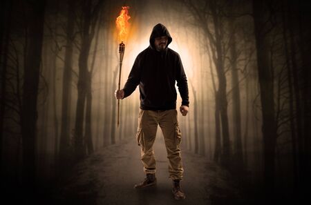 Mysterious man coming from a path in the forest with burning flambeau concept