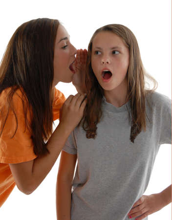 Teenage girls sharing secrets. One girl whispering gossip in the ear of the other girl who is shocked at the information she is getting. Studio white background. - 10756969